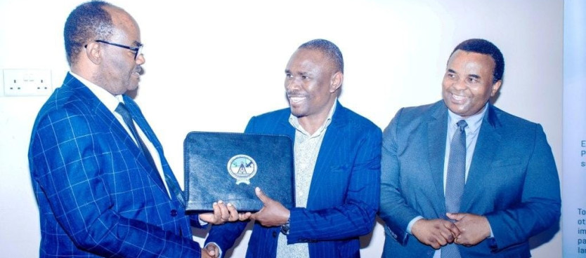 Waziri wa Ardhi, Numba na Maendeleo ya Makazi Mhe. Dkt. Leonard Akwilapo akimkabidhi vitendea kazi mmoja wa Wajumbe wa Kamati ya Ufundi ya Mipango ya Matumizi ya Ardhi katika tukio la uzinduzi wa Kamati hiyo lililofanyika Jijini Dodoma 17/12/2025